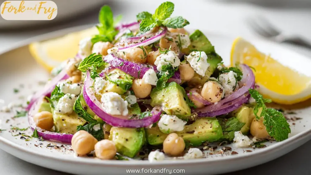 Chickpea avocado feta salad in a white bowl with herbs and lemon slices