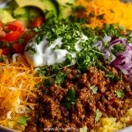 vibrant taco rice bowl with ground beef, shredded cheese, red onion, tomato, avocado, and sour cream