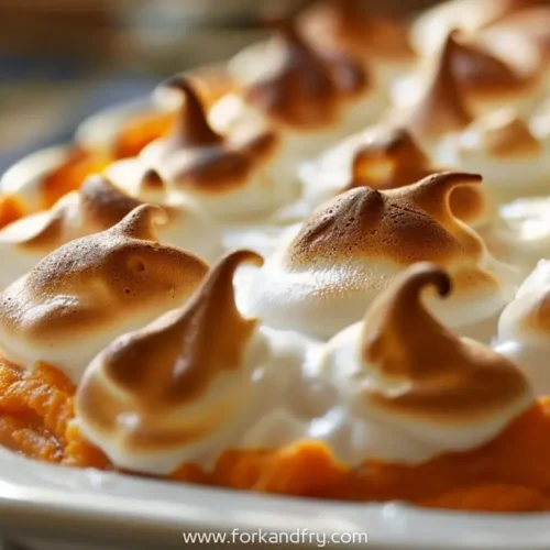 Golden meringue topped sweet potato casserole with melted marshmallows in white dish.