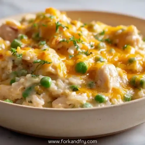 Cheesy chicken and rice casserole with peas in a beige bowl, topped with fresh herbs