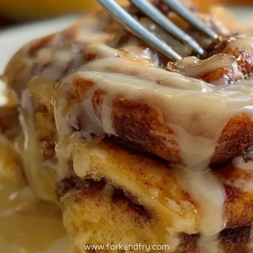 gooey cinnamon roll topped with creamy vanilla glaze and fork about to slice