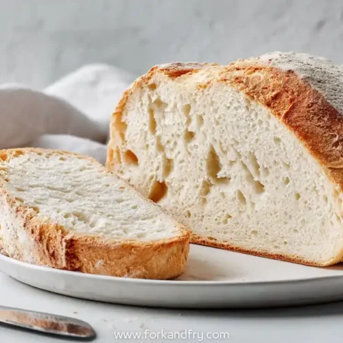 sliced crusty homemade bread on white plate with soft interior and golden brown crust