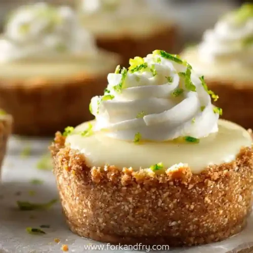 Mini key lime tartlets with whipped cream topping and lime zest on a rustic surface