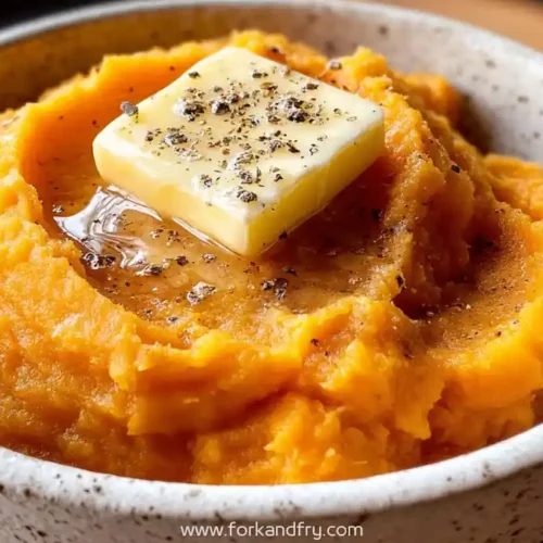 Creamy mashed sweet potatoes topped with melting butter and cracked black pepper in a rustic ceramic bowl