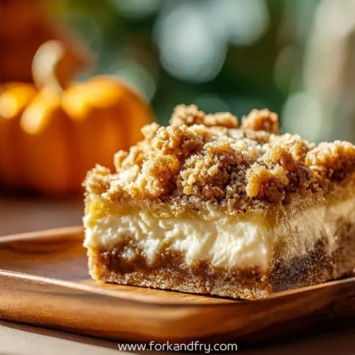 close-up of pumpkin cheesecake crumb bar on wooden plate with mini pumpkins in background