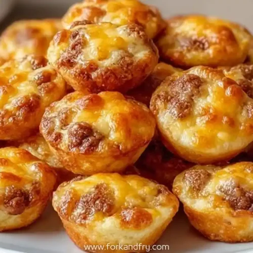 golden-brown sausage egg muffins stacked on a white plate, topped with melted cheese