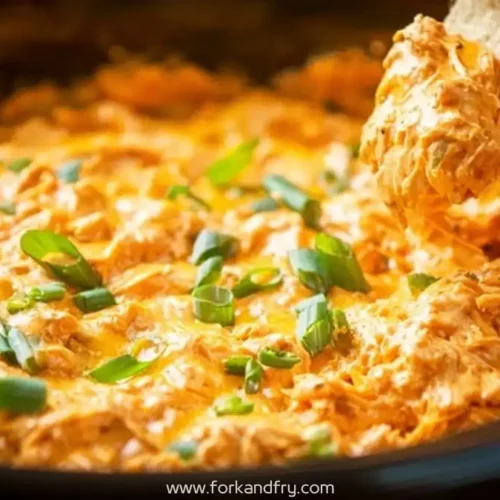 hot and cheesy buffalo chicken dip topped with green onions being scooped with a tortilla chip