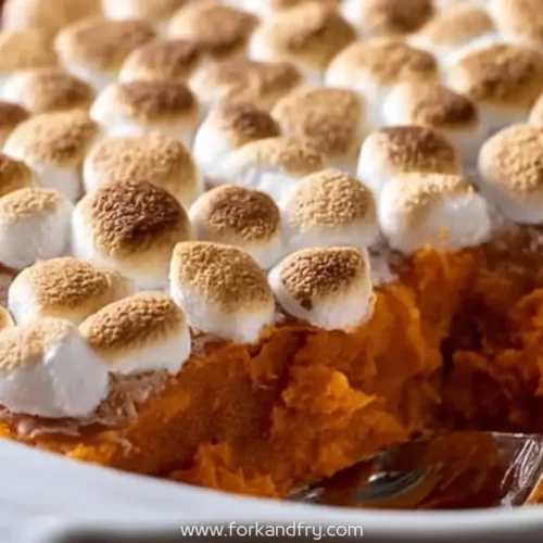 sweet potato casserole topped with toasted marshmallows in white dish with spoon
