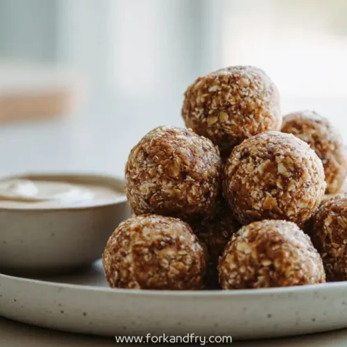 Apple cinnamon energy bites stacked on a ceramic plate with creamy dipping sauce