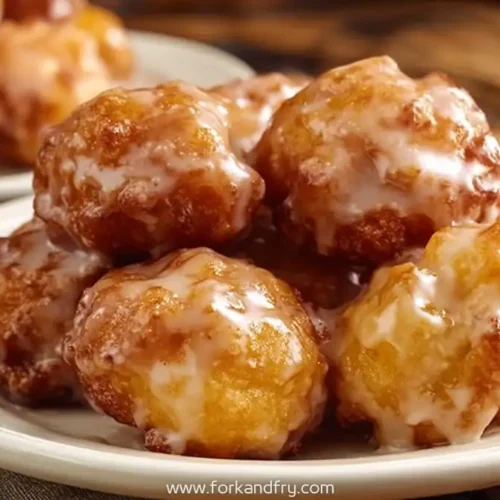 Glazed apple fritter bites stacked on a white plate, golden brown and shiny with sweet icing