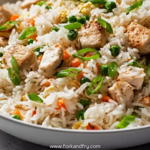Chicken and vegetable fried rice with green peas, carrots and scallions in a white bowl