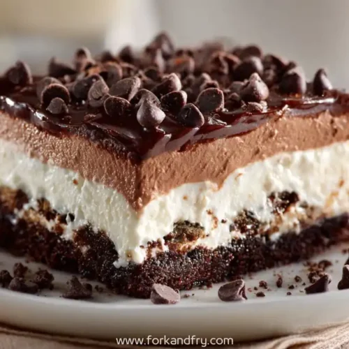 Layered no-bake chocolate lasagna cake with whipped cream, mousse, and chocolate chips on a white plate
