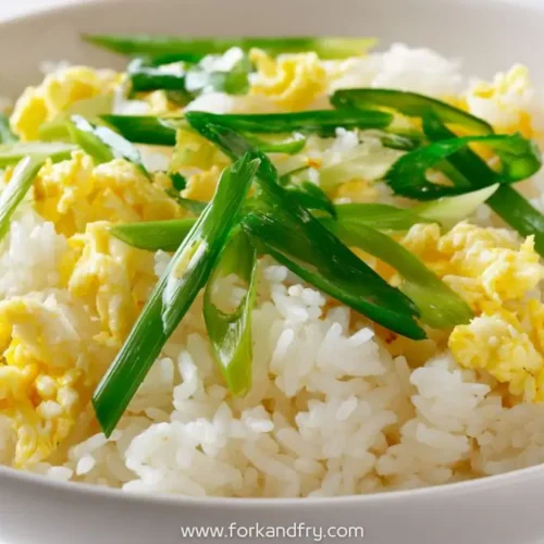 Fluffy egg fried rice topped with sliced scallions in a white bowl