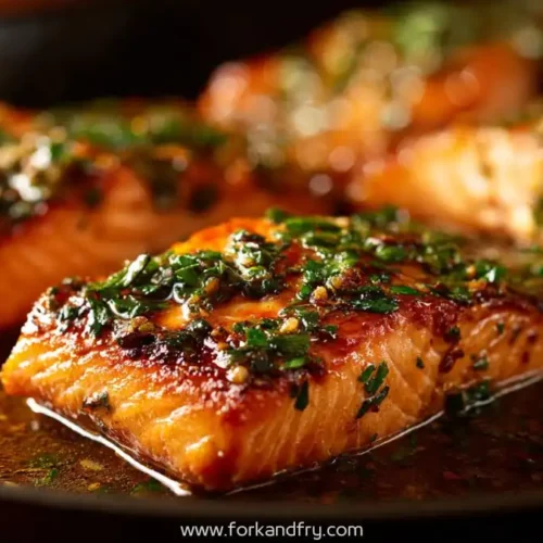 Seared garlic butter salmon fillets in skillet with herbs and golden sauce glaze
