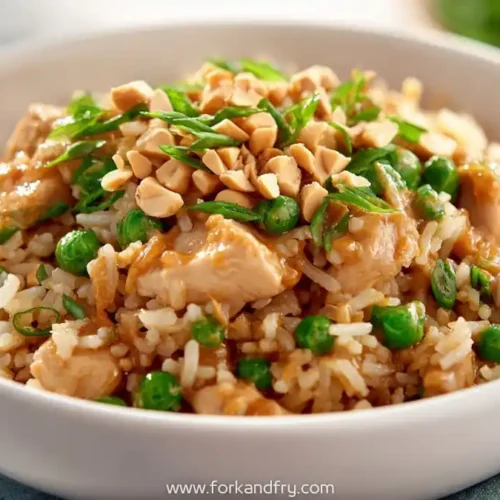 Peanut chicken fried rice with green peas, chopped peanuts, and scallions in a white bowl