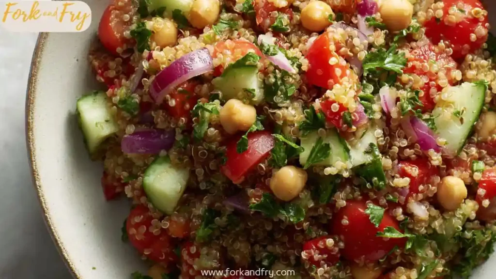 Quinoa salad with chickpeas, cucumber, cherry tomatoes, red onion, and parsley in a white bowl