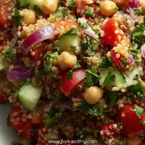 Quinoa salad with chickpeas, cucumber, cherry tomatoes, red onion, and parsley in a white bowl