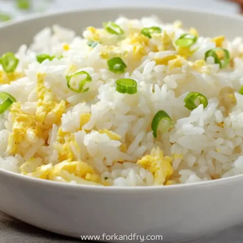 Simple egg fried rice with scallions in a white bowl on a neutral background