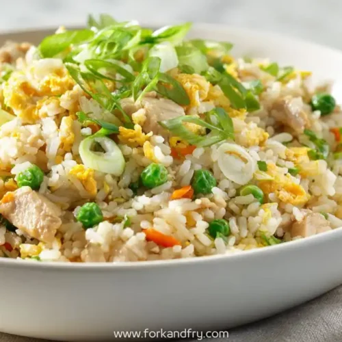 loseup of weeknight chicken fried rice with scrambled eggs, peas, scallions and tender chicken in a white bowl