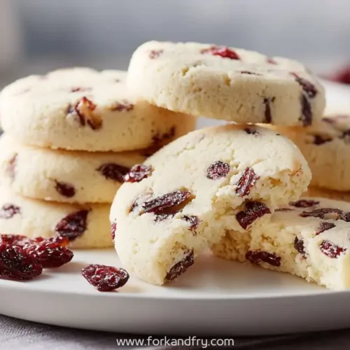 buttery cranberry shortbread cookies stacked on plate with one broken cookie showing soft texture