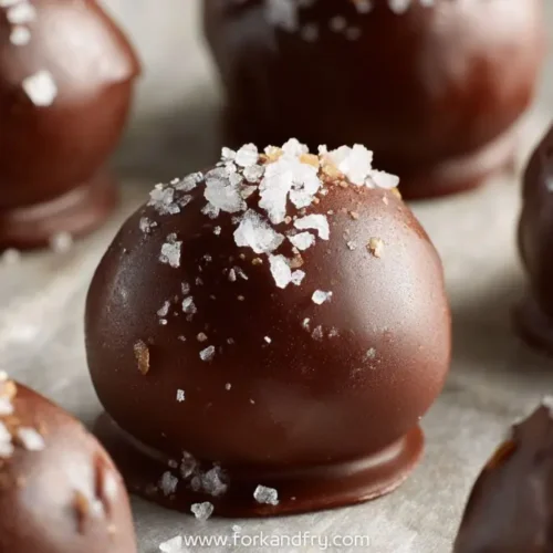 Chocolate-coated peanut butter truffles topped with flaky sea salt on parchment