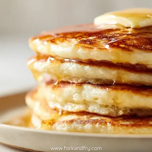 Stack of fluffy cottage cheese pancakes topped with melting butter and maple syrup on a beige plate