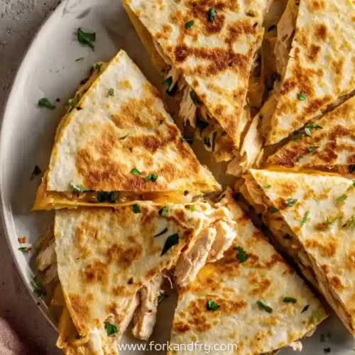 golden crispy chicken quesadilla wedges on plate with fresh herbs