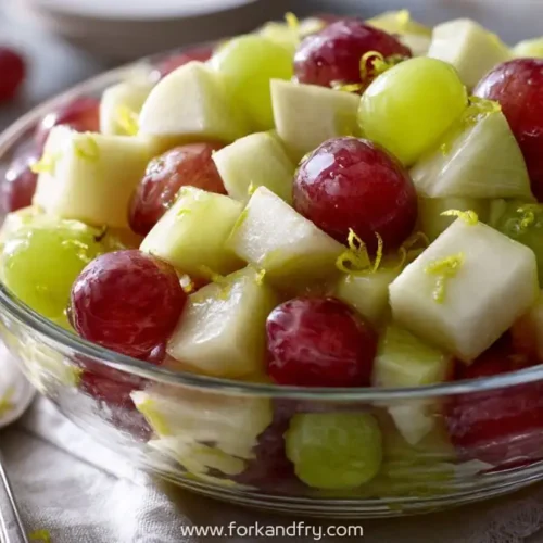 Glass bowl filled with red grapes, green grapes, apple cubes and lemon zest on rustic table
