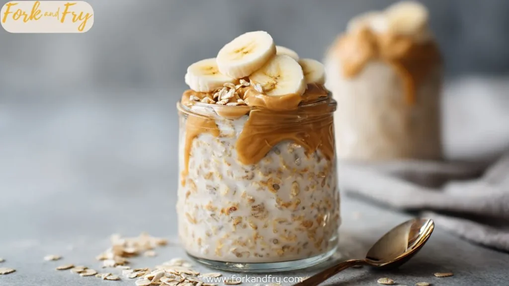 Overnight oats in a glass jar topped with banana slices, peanut butter, and oats on a grey background