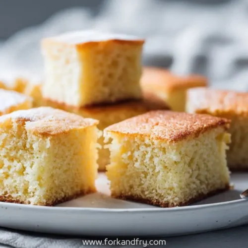 Golden sponge sheet cake cut into fluffy squares and served on a round white plate