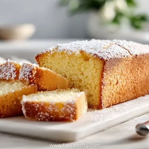 Golden loaf cake sliced on a white board dusted with powdered sugar and served with yogurt