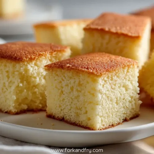Squares of golden snack cake without frosting on a white plate, ready to serve