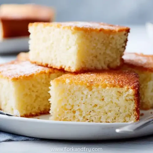 Golden vanilla snack cake slices stacked on a white plate with soft crumb