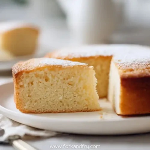 Moist vanilla cake dusted with powdered sugar on white plate with slice cut out