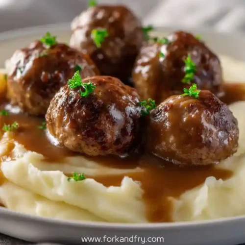 beef meatballs with brown gravy over creamy mashed potatoes garnished with parsley
