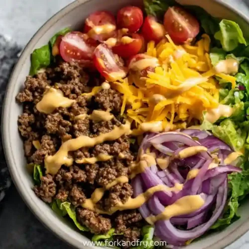 High protein cheeseburger bowl with ground beef, cheddar cheese, cherry tomatoes, red onion, lettuce and creamy burger sauce