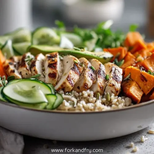Healthy chicken bowl with grilled chicken slices, brown rice, cucumber, shredded carrots, roasted sweet potatoes, and fresh herbs in a balanced meal bowl.