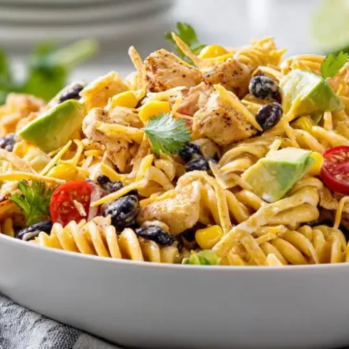 Creamy chicken pasta salad with avocado, black beans, corn, cherry tomatoes, and tortilla strips in a white bowl
