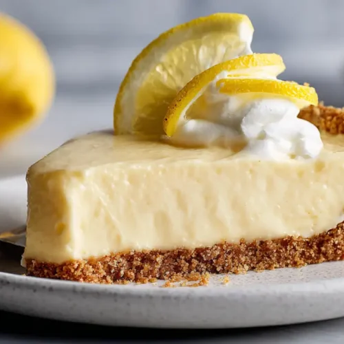 Slice of chilled lemon refrigerator pie topped with whipped cream and lemon slices on a graham cracker crust served on a plate.