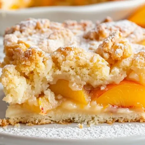 Warm peach dump cake topped with powdered sugar and fresh peach slices on a dessert plate