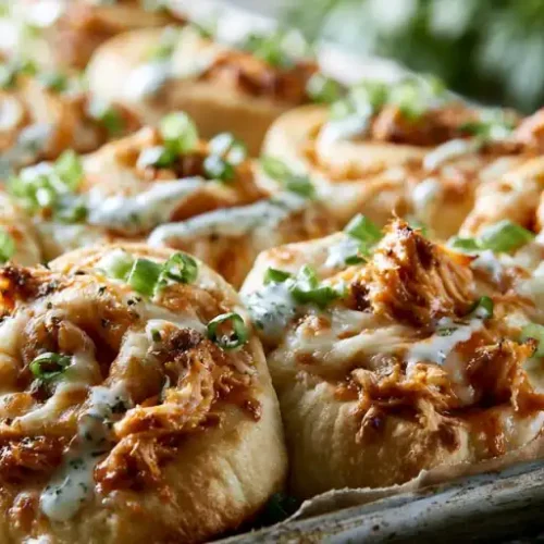Cheesy Buffalo chicken pizza rolls baked until golden brown and topped with ranch dressing and sliced green onions.