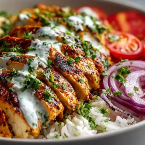 Chicken shawarma rice bowl topped with garlic yogurt sauce, cucumber, tomatoes, red onion, and fluffy white rice.