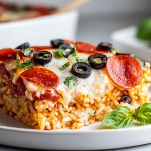 Loaded pizza rice bake topped with pepperoni, melted mozzarella, black olives, and fresh basil served on a white plate.