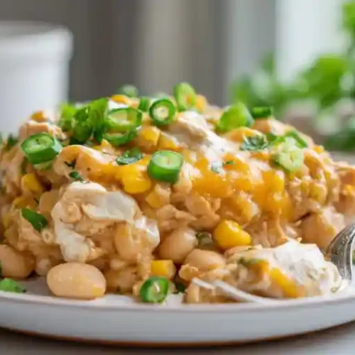 A serving of creamy chicken chili bake topped with melted cheddar, white beans, corn, sliced green onions, and fresh cilantro on a white plate.