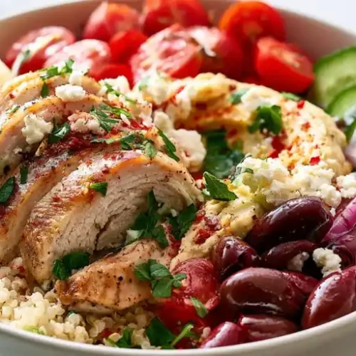 Grilled chicken hummus bowl with quinoa, cherry tomatoes, cucumber, red onion, Kalamata olives, feta cheese, parsley, and a lemon wedge.