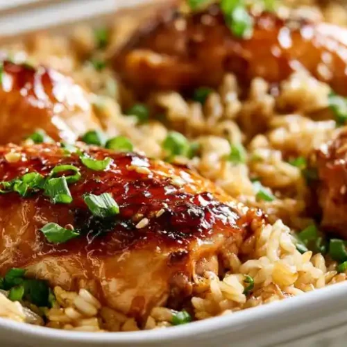 Sticky honey glazed chicken baked over seasoned rice in a casserole dish, garnished with chopped green onions.